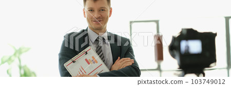 Male business coach standing in front of camera with documents in hands 103749012