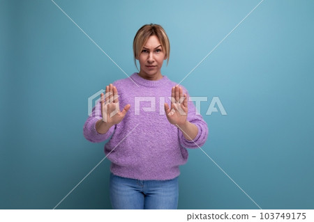blonde woman in purple hoodie showing stop sign with hands on blue background 103749175