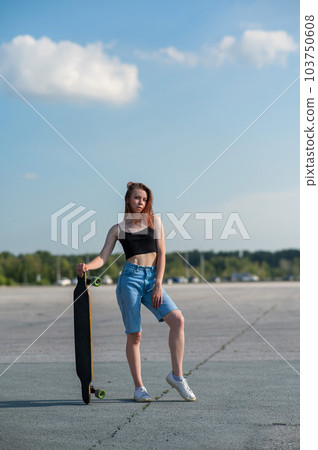 Young caucasian woman holding a long board outdoors.  103750608