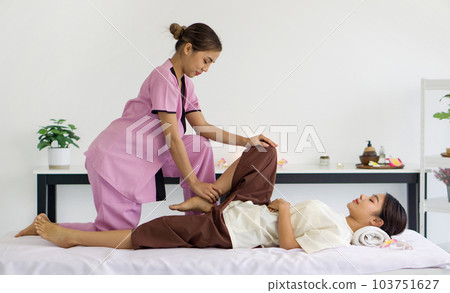 Body care treatment by thai massage. Cute girl with traditional dress stretch knee and leg by massager. Young asian woman relax in spa. Body care treatment by thai massage. Cute girl with traditional dress stretch knee and leg by massager. Young asian woman relax in spa. 103751627