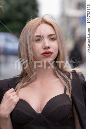 Portrait of elegant lady in business suit walks around the city. Young woman is blonde with deep neckline. Vertical frame. 103752128