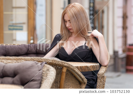 Portrait beautiful business woman with blonde hair in black suit sitting on table in cafe outside and waiting her order. 103752130