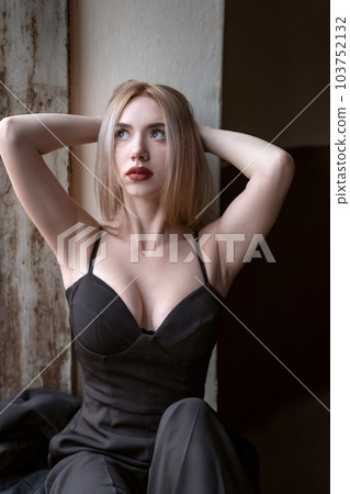 Attractive young blonde woman wears black top with deep sweetheart neckline with her hands behind head. Girl with seductive figure. 103752132