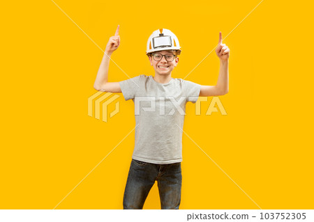 Cheerful smiling teenage guy wears t-shirt jeans and protective helmet points his index fingers up. Copy space. Space for text. 103752305