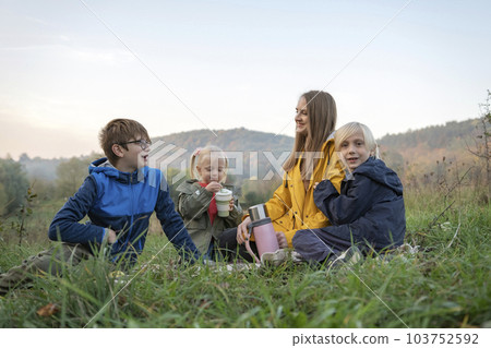 Happy young family on picnic communicate and smiling. Three siblings with mother resting on the nature Happy young family on picnic communicate and smiling. Three siblings with mother resting on the nature 103752592