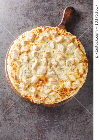 Pizza with creamy homemade alfredo sauce topped with chicken, mozzarella and parmesan cheese closeup on the wooden board. Vertical top view 103753617