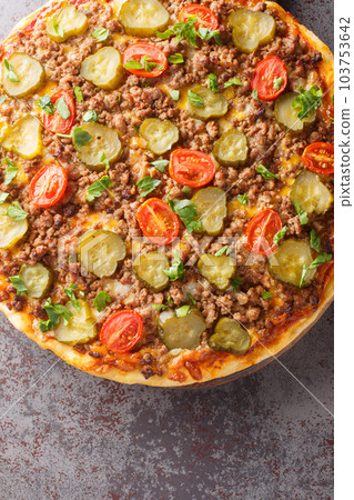 Delicious hot hamburger pizza with ground beef, tomatoes, pickles and cheese close-up on a wooden board on the table. Vertical top view Delicious hot hamburger pizza with ground beef, tomatoes, pickles and cheese close-up on a wooden board on the table. Vertical top view 103753642