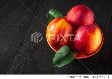 Three red ripe nectarine hybrids in their ripening season lie on orange plate or on a dark vintage table. Three red ripe nectarine hybrids in their ripening season lie on orange plate or on a dark vintage table. 103754281