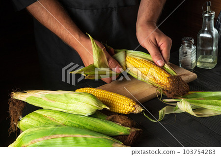 Professional chef peels ripe corn from the shell before cooking. Working environment in the restaurant kitchen. The hands of the cook close-up while working 103754283