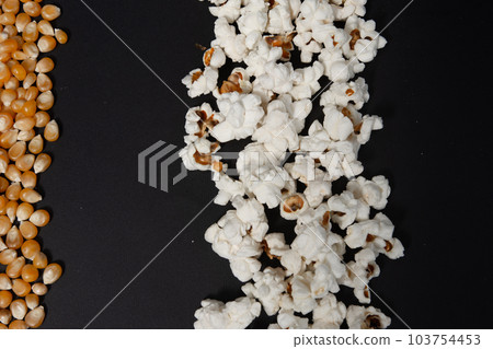 a row of ready-made popcorn and a row of corn kernels on a black background, place for inscription and advertising. 103754453