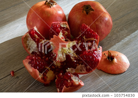 Two fresh ripe pomegranates and one cut on a gray wooden table Two fresh ripe pomegranates and one cut on a gray wooden table 103754830