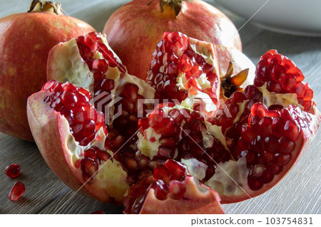 Two fresh ripe pomegranates and one cut on a gray wooden table Two fresh ripe pomegranates and one cut on a gray wooden table 103754831
