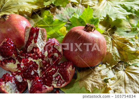 Two fresh ripe pomegranates and one cut on yellow autumn leaves Two fresh ripe pomegranates and one cut on yellow autumn leaves 103754834