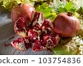 Two fresh ripe pomegranates and one cut on a gray wooden table and yellow autumn leaves 103754836