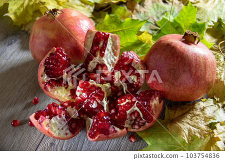 Two fresh ripe pomegranates and one cut on a gray wooden table and yellow autumn leaves 103754836