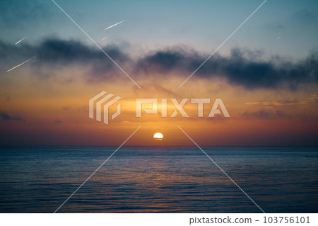 The sun rises over the a calm sea with dark clouds in the foreground 103756101