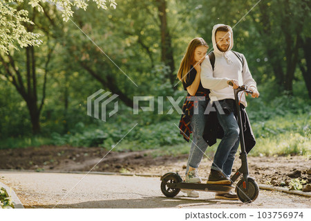 Tourists in a summer forest. Girl in a black t-shirt. Electric scooter. Tourists in a summer forest. Girl in a black t-shirt. Electric scooter. 103756974