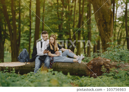 Tourists in a summer forest. Girl in a black t-shirt. Man use a phone. Tourists in a summer forest. Girl in a black t-shirt. Man use a phone. 103756983