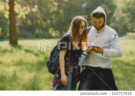 Tourists in a summer forest. Girl in a black t-shirt. Man use a phone. 103757018