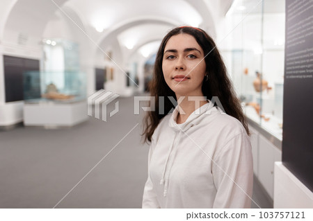 Portrait of young smiling caucasian woman posing in museum. Light hall in background. Concept of cultural education and Museum's Day 103757121