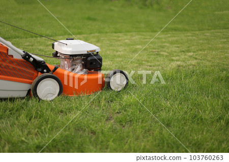 Close up orange-grey electric lawn mower on bright lush green lawn. Gardening work tools. Rotary lawn mower machine cut grass. Professional lawn care service. Place for text Close up orange-grey electric lawn mower on bright lush green lawn. Gardening work tools. Rotary lawn mower machine cut grass. Professional lawn care service. Place for text 103760263