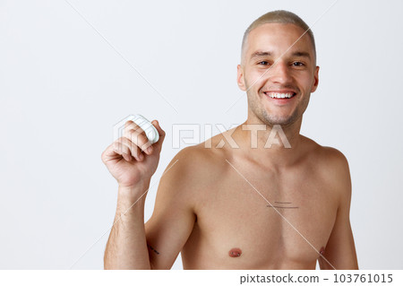 Portrait of handsome young man with well-kept skin, posing shirtless, using deodorant against white studio background 103761015
