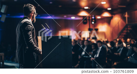 Speaker giving a talk on corporate business conference. Unrecognizable people in audience at conference hall. Business and Entrepreneurship event. Speaker giving a talk on corporate business conference. Unrecognizable people in audience at conference hall. Business and Entrepreneurship event. 103761809