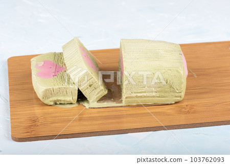 Sliced pistachio ice cream with a raspberry heart-shaped layer on a cutting board. 103762093