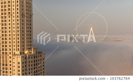 Bluewaters island with modern architecture and ferris wheel covered by morning fog aerial timelapse. Bluewaters island with modern architecture and ferris wheel covered by morning fog aerial timelapse. 103762764