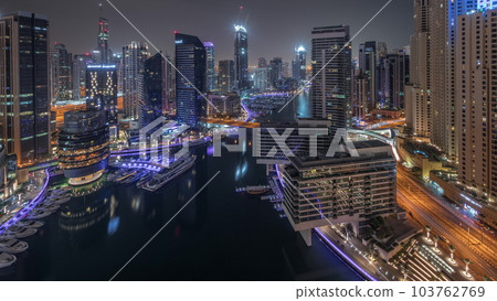 Aerial view to Dubai marina skyscrapers around canal with floating boats all night timelapse Aerial view to Dubai marina skyscrapers around canal with floating boats all night timelapse 103762769