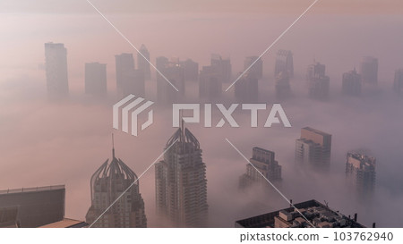 Fog covered JLT skyscrapers and marina towers near Sheikh Zayed Road aerial timelapse during sunrise. Residential buildings 103762940
