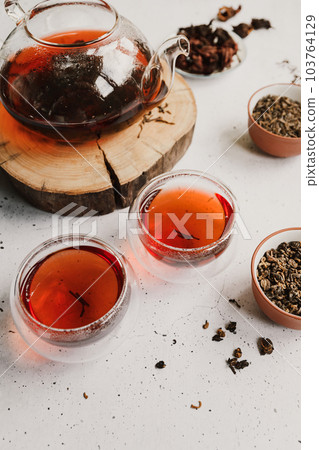Different types of tea. Black, green and hibiscus sorts on a white table with teapot and glasses. Different types of tea. Black, green and hibiscus sorts on a white table with teapot and glasses. 103764129