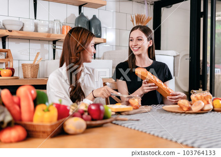Two young woman slicing bread with knife on wooden cutting board 103764133