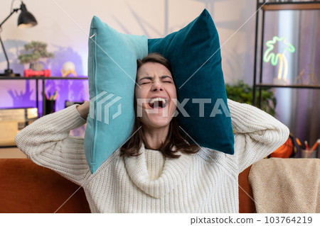Repair work at neighbours concept, irritated woman at home cover ears with pillows annoyed by noise Repair work at neighbours concept, irritated woman at home cover ears with pillows annoyed by noise 103764219