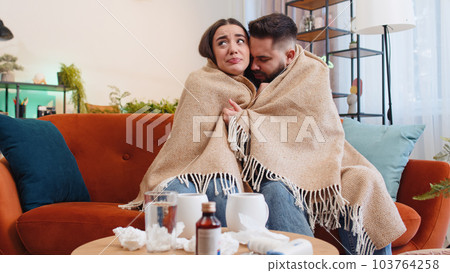 Sick ill family man woman suffering from cold sitting on home couch sneezes wipes snot into napkin 103764258