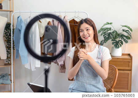 Female online seller is using smartphone to broadcast live on Vlog for introduce new fashions and talking 103765003