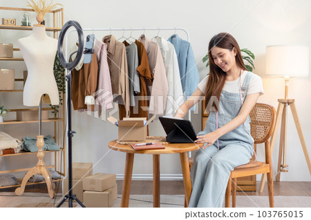 Female online seller is checking online clothes orders on tablet after using smartphone to broadcast live Female online seller is checking online clothes orders on tablet after using smartphone to broadcast live 103765015
