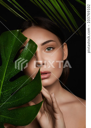 beautiful girl behind the palm. Beautiful young woman with Make-up 103769102