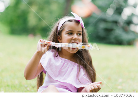 Cute baby girl in pink dress eats white cotton candy in the park in summer 103770163