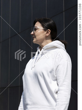 Portrait Pretty Mature Brunette Woman in White Hoodie and Sunglasses Looks Away, Dark Background Wall. Sportive Confident 40 Yo Beautiful Caucasian Woman in City. Vertical Plane 103771108