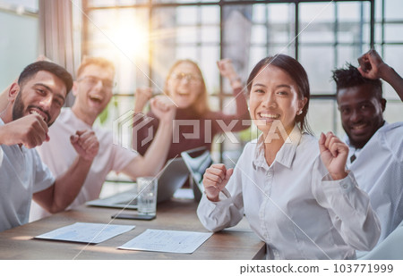 group of different business people celebrating victory while sitting at table in modern office group of different business people celebrating victory while sitting at table in modern office 103771999