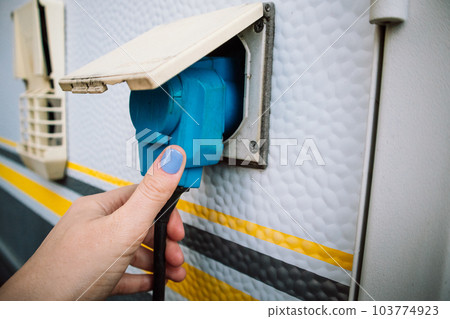 Industrial electrical box for caravan. Power supply. Motorhome charge connecting to voltage. Camper parking charging in female hand. A woman charging a car with electricity. Mobile home electricity. Industrial electrical box for caravan. Power supply. Motorhome charge connecting to voltage. Camper parking charging in female hand. A woman charging a car with electricity. Mobile home electricity. 103774923