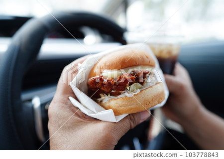 Asian woman driver hold and eat hamburger in car, dangerous and risk an accident. Asian woman driver hold and eat hamburger in car, dangerous and risk an accident. 103778843