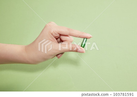 A female hand holding a single a green capsule of vitamin on a light green background. Drug concept with space to copy. 103781591