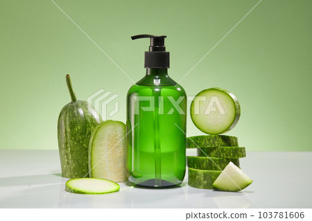 Front view of a green bottle unbranded with fresh winter melon slices displayed on green background. Mockup scene for advertising product, shampoo, shower gel or body lotion with winter melon extract Front view of a green bottle unbranded with fresh winter melon slices displayed on green background. Mockup scene for advertising product, shampoo, shower gel or body lotion with winter melon extract 103781606