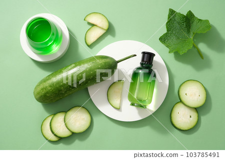 Scene for advertising and branding cosmetic product of winter melon extract. Glass bottle and glass cup filled green liquid on podium, decorated with fresh winter melon on green background.  103785491
