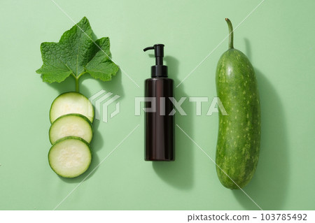 Minimal flat lay scene for advertising - an amber pump bottle with fresh winter melon, slices and leaf decorated on a light green background. Advertising scene for cosmetic skin care and body care Minimal flat lay scene for advertising - an amber pump bottle with fresh winter melon, slices and leaf decorated on a light green background. Advertising scene for cosmetic skin care and body care 103785492