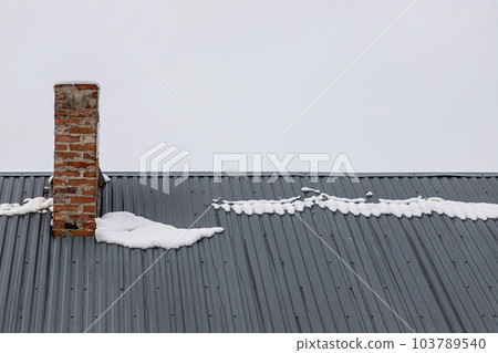 a brick chimney on a metal roof in the winter under the snow. construction concept 103789540