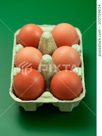 Brown raw organic eggs with yolk inside in paper tray on green. 103789614