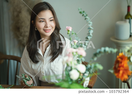 Pretty young woman small business owner preparing bouquet of pink flowers at tablet in her flower shop 103792364